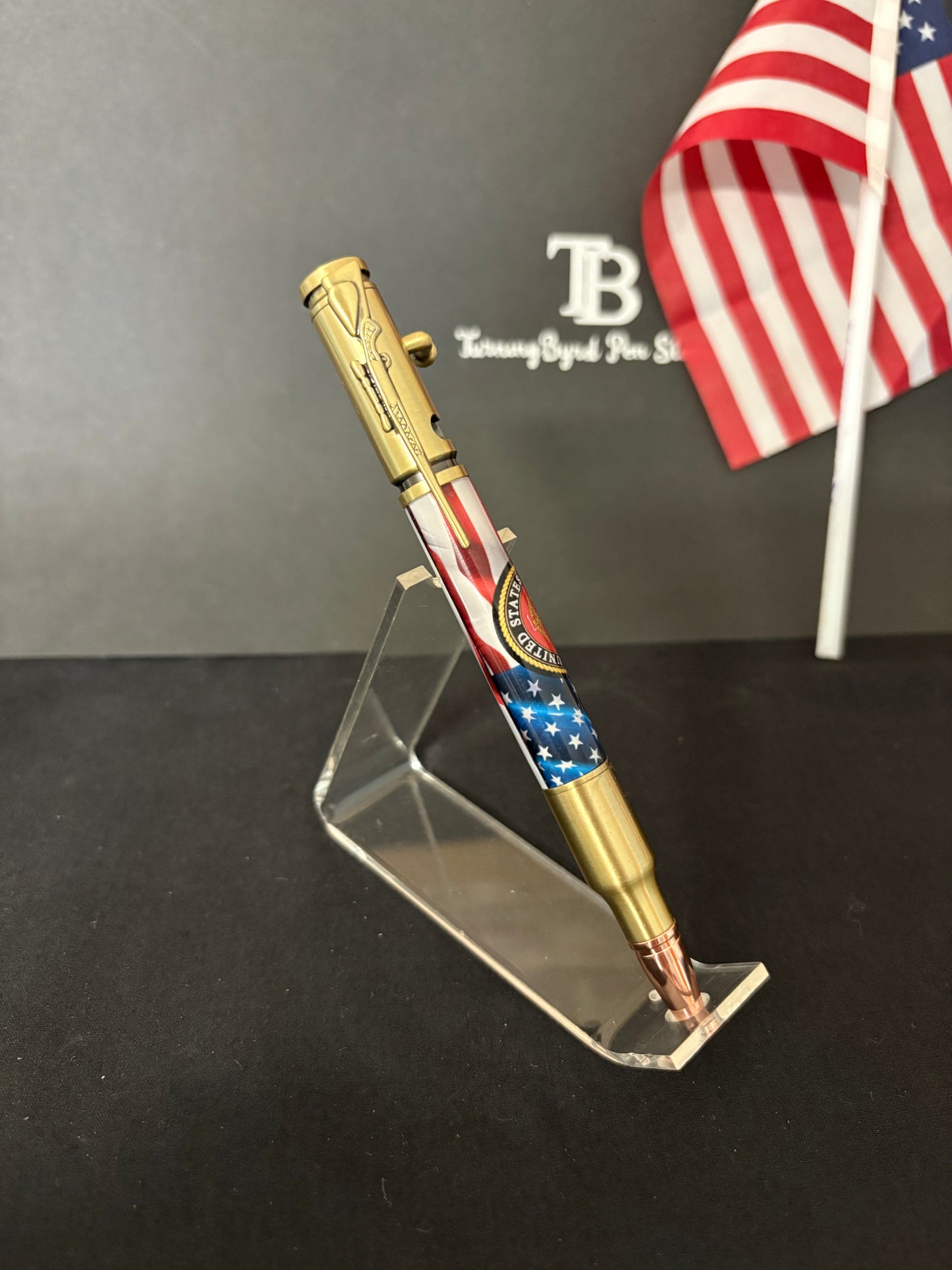 USMC Bolt Action Ballpoint pen with American flag design on a stand against a dark background