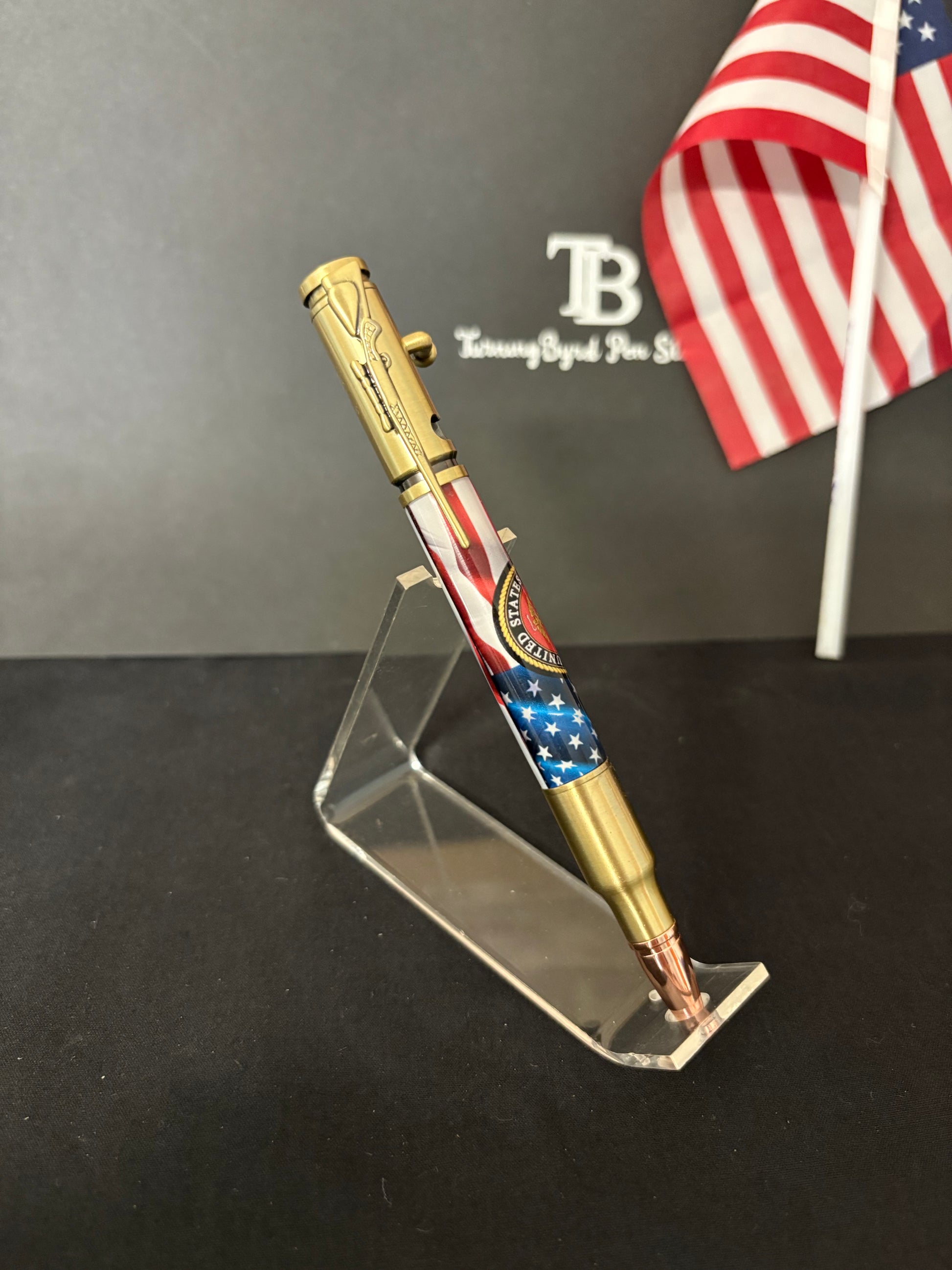 USMC Bolt Action Ballpoint pen with American flag design on a stand against a dark background