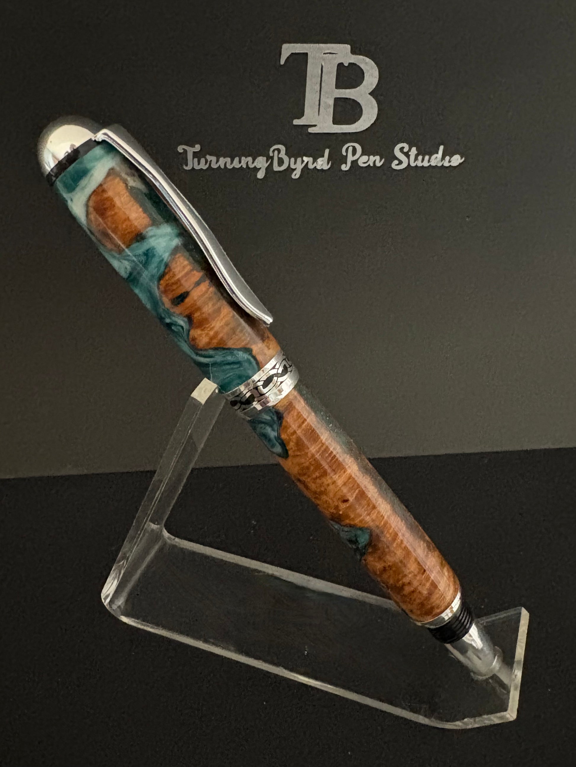 Cherry Burl Wood pen with green and white resin on a clear stand against a gray background with 'TB Turning Byrd Pen Studio' logo.