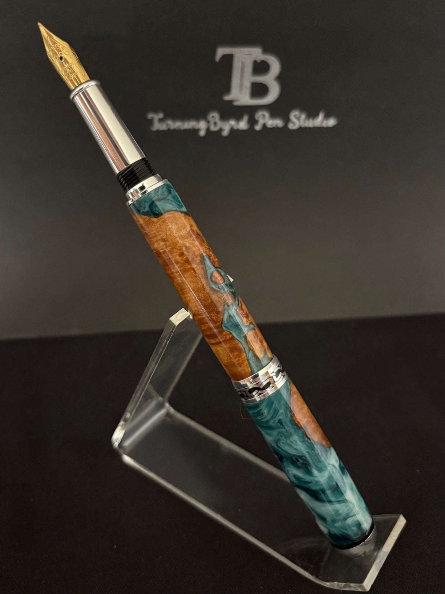Cherry Burl Wood pen with green and white resin on a clear stand against a gray background with 'TB Turning Byrd Pen Studio' logo.
