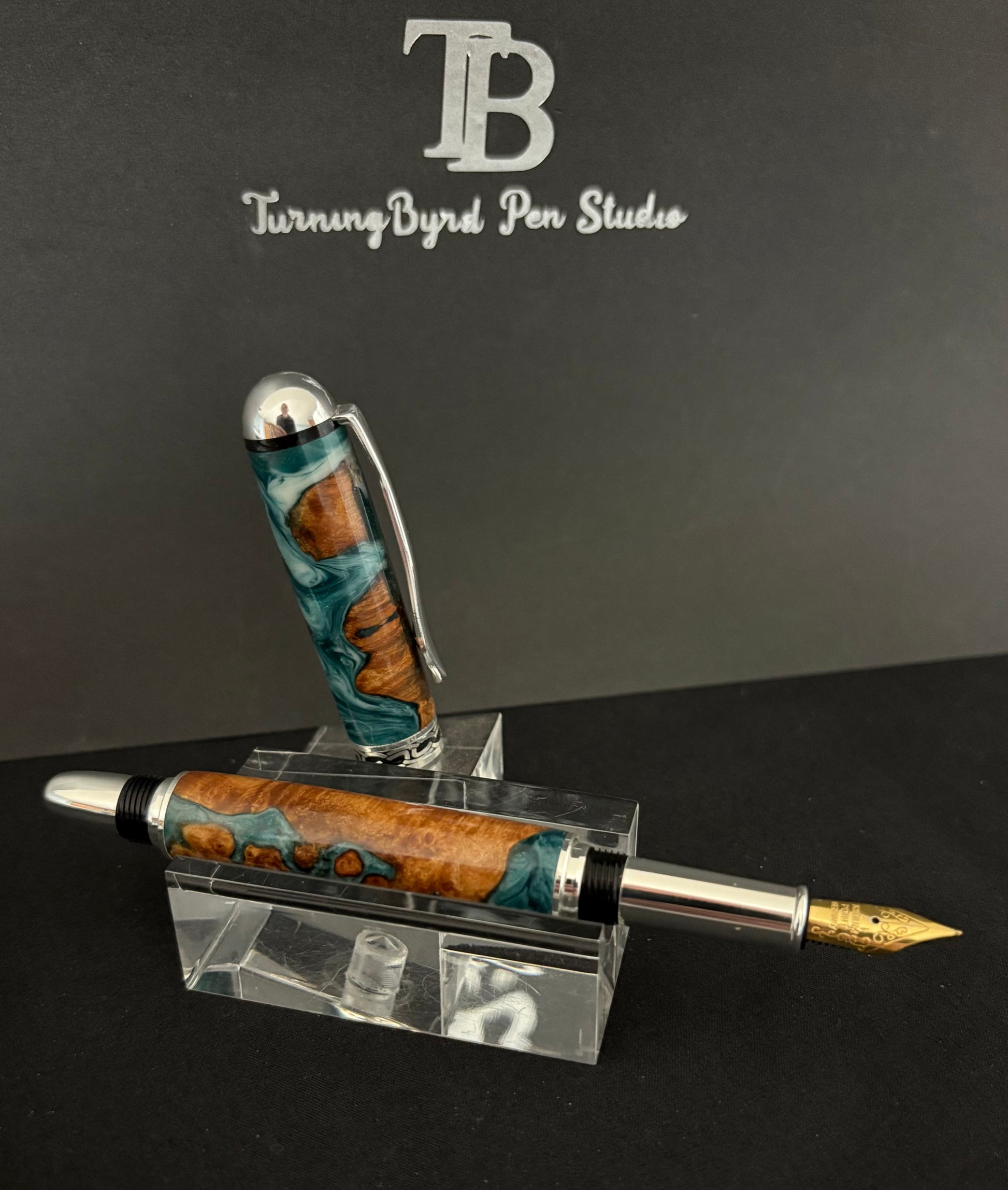 Cherry Burl Wood pen with green and white resin on a clear stand against a gray background with 'TB Turning Byrd Pen Studio' logo.