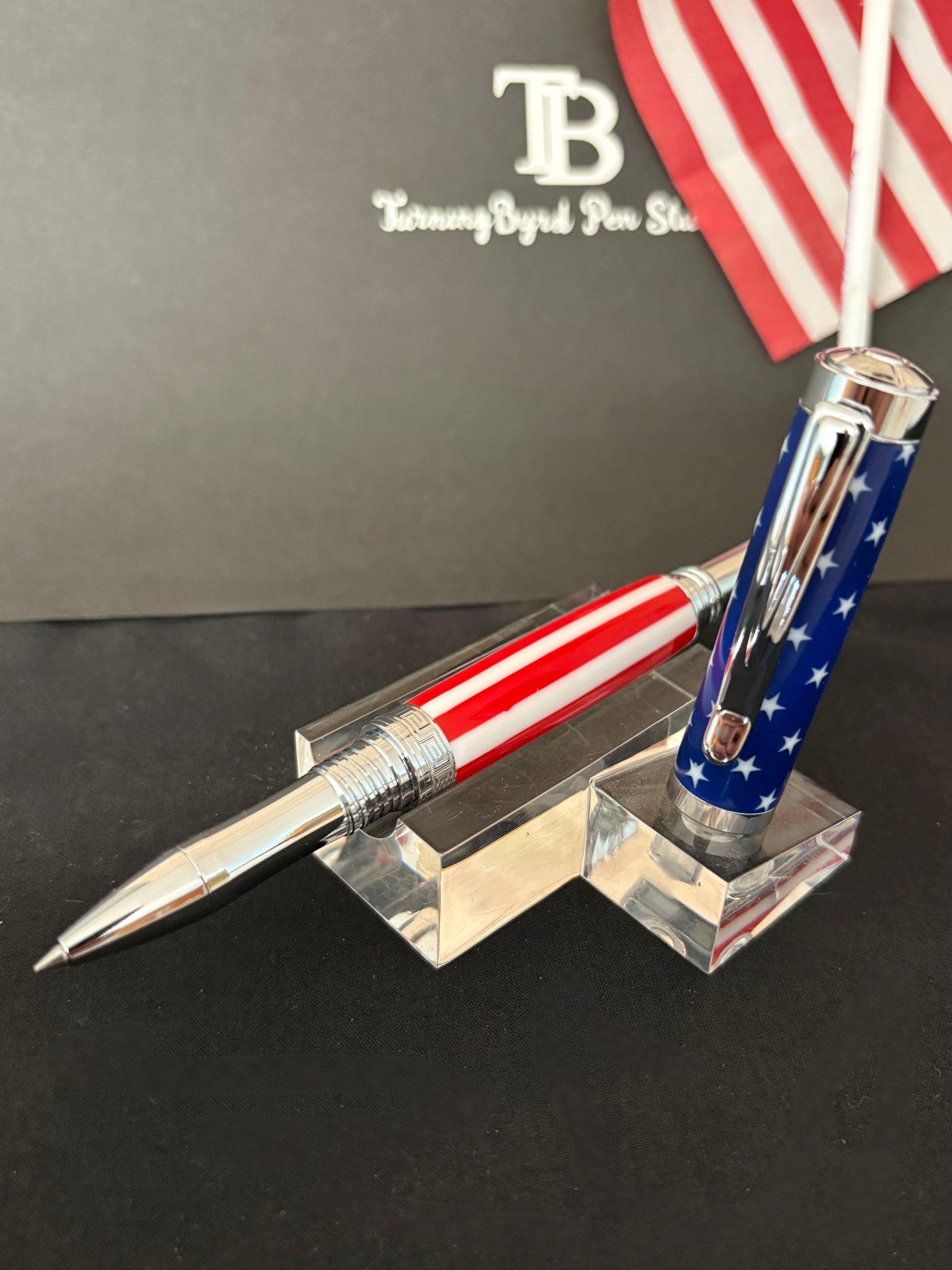 Stars and Stripes Rollerball Pen with American flag design on a stand, with TurningByrd Pen Studio branding in the background.