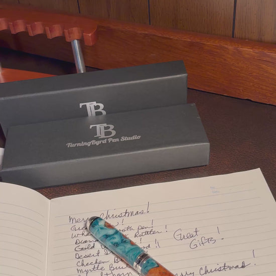 Cherry Burl Wood pen with green and white resin on a clear stand against a gray background with 'TB Turning Byrd Pen Studio' logo.